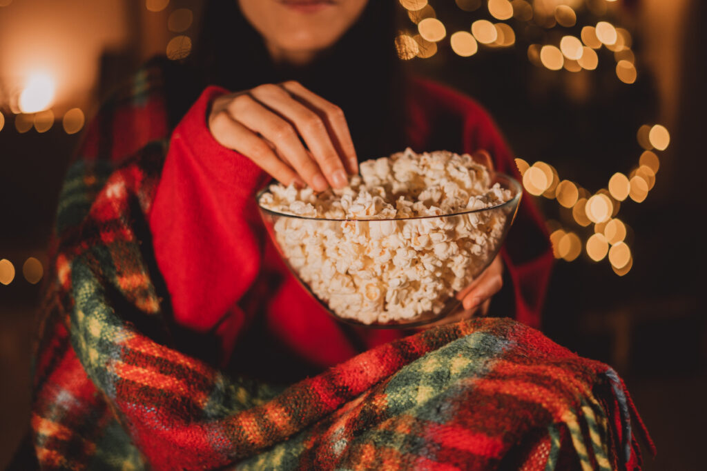 Woman eating popcorn and watching Christmas TV at home.